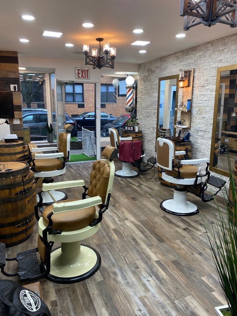 Inside a barbershop with leather chairs, wooden barrel, and wide windows