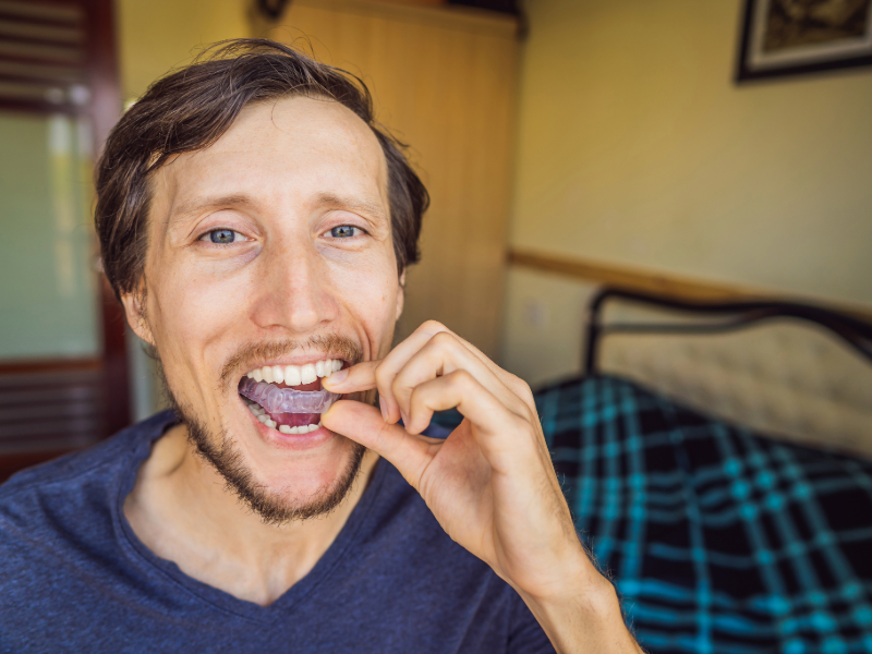 Man placing a custom nightguard onto his teeth, demonstrating how nightguards help protect against grinding