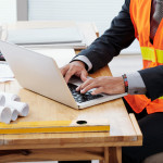 unrecognizable-man-neon-safety-vest-business-suit-sitting-desk-using-laptop (1)-min.jpg