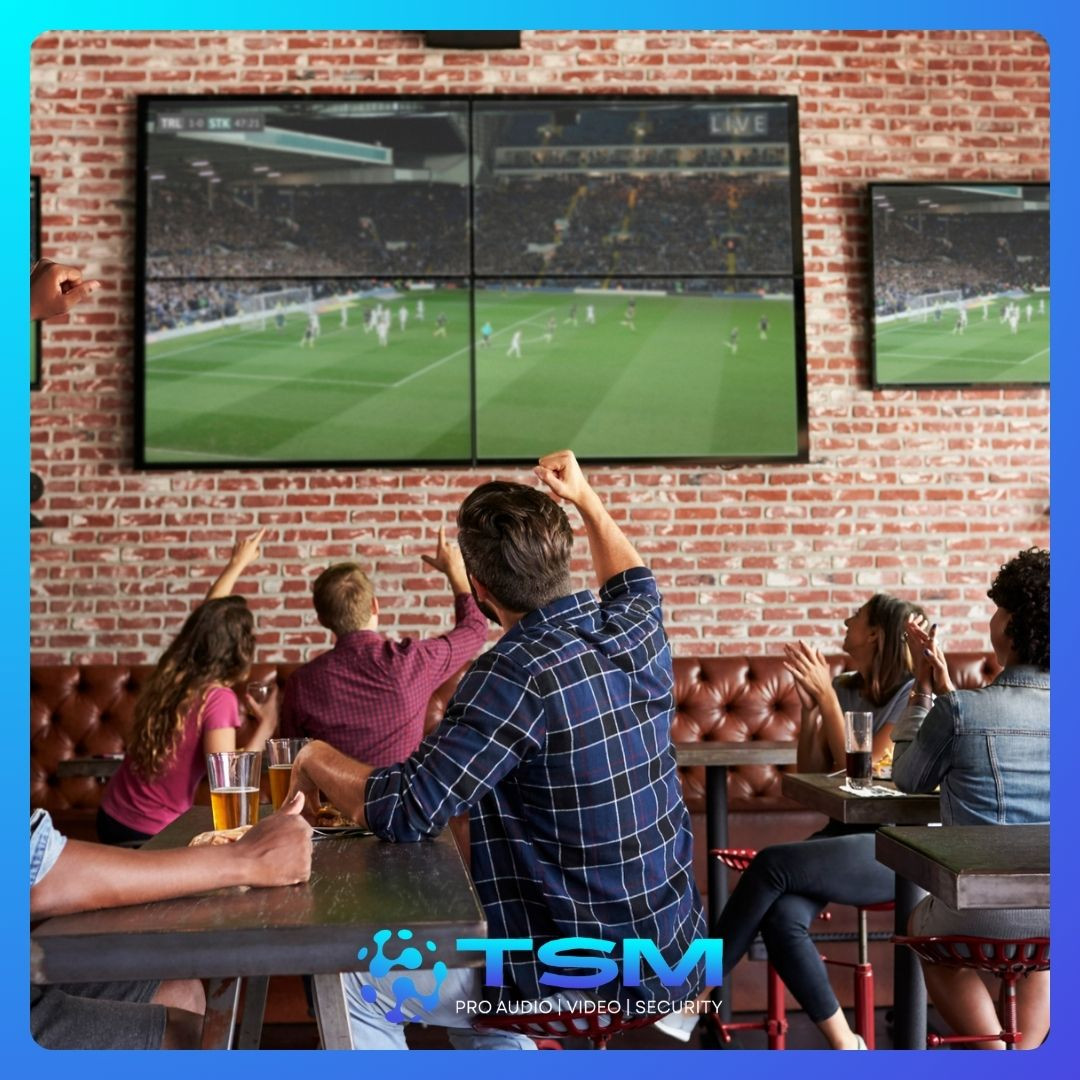 Group of people watching a sports game on multiple large screens in a bar