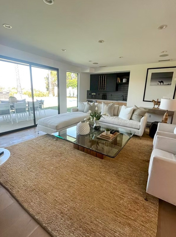 Bright, spacious living room with white furniture, a large glass coffee table, and sliding doors to a patio.