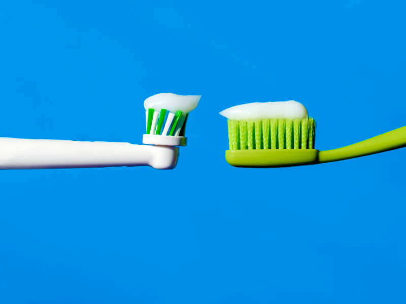 Side-by-side comparison of a manual toothbrush and an electric toothbrush head with toothpaste, illustrating differences in brushing technology.