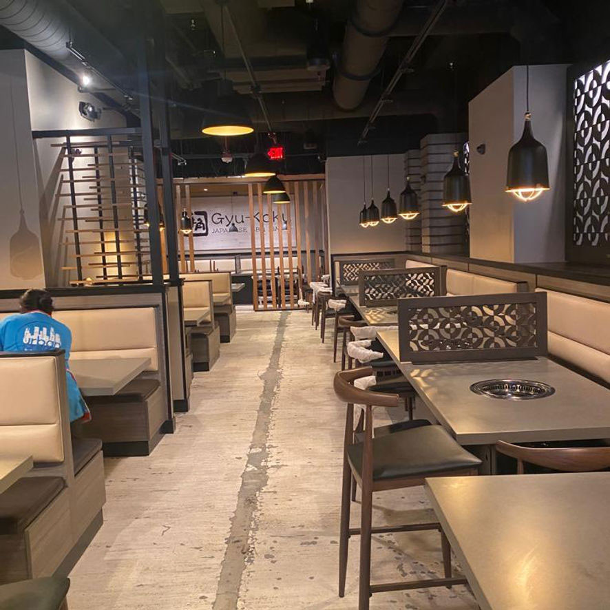 The interior of a Gyu-Kaku restaurant shows clean, empty dining tables with built-in grills and stylish pendant lighting.