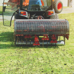 gardener operating soil aeration machine on grass lawn.jpg