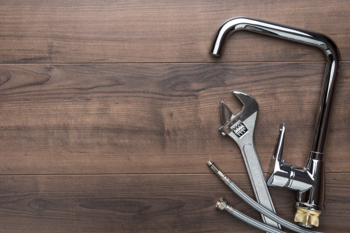 Wooden board with an uninstalled faucet and wrenches on it