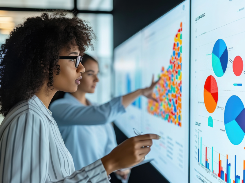 Two business professionals analyzing colorful data dashboards with charts and graphs, representing data-driven marketing decisions and measurable ROI from aligned sales and marketing systems.
