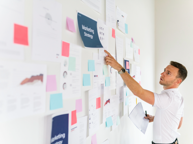 B2B marketing professional analyzing strategy board covered with charts, reports, and sticky notes during a marketing system audit.