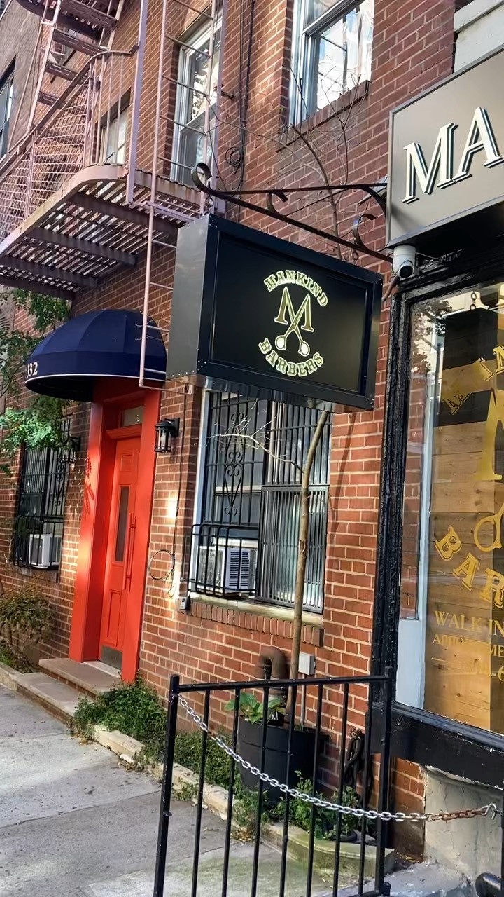 Exterior of Mankind Barbers with a black and gold hanging sign on a brick building.