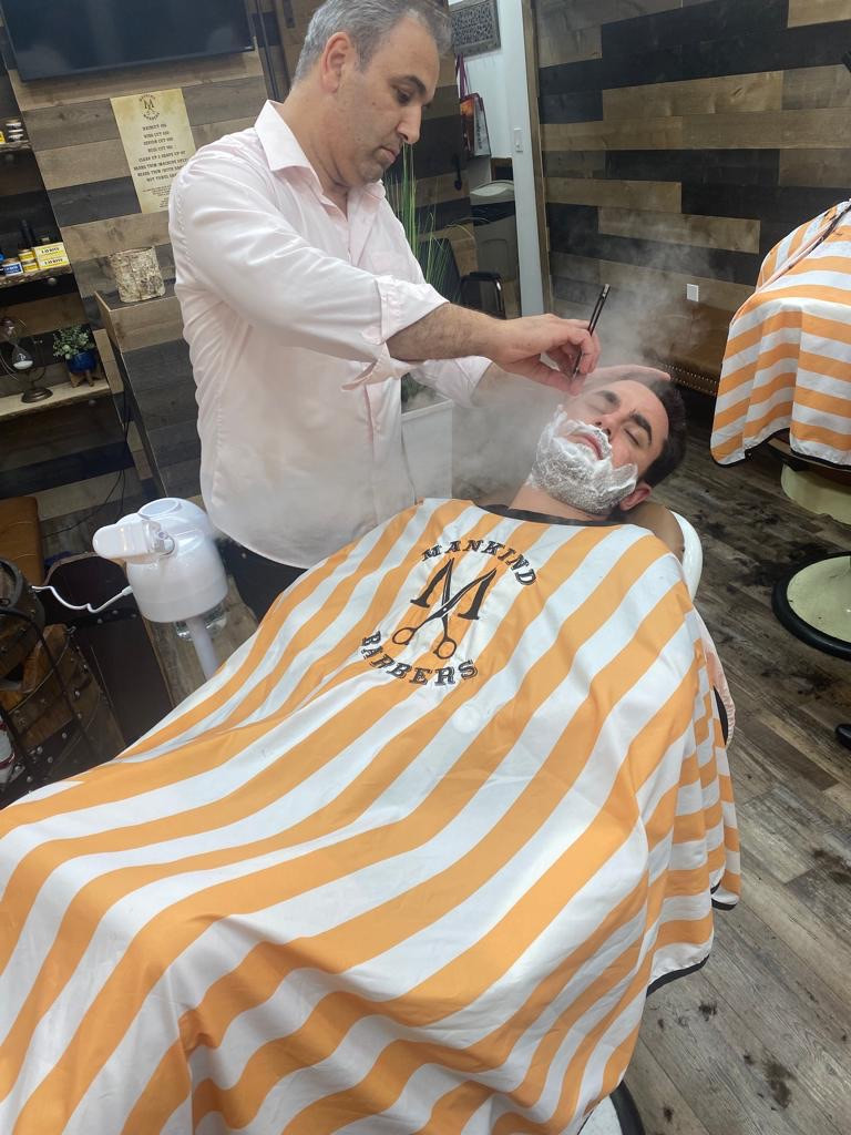 Barber giving a hot towel shave to a client with shaving cream