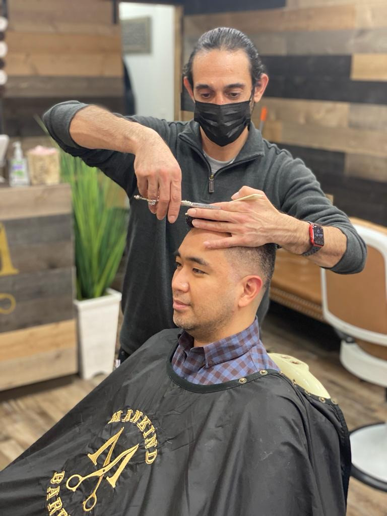 Barber wearing a mask giving a haircut to a seated customer